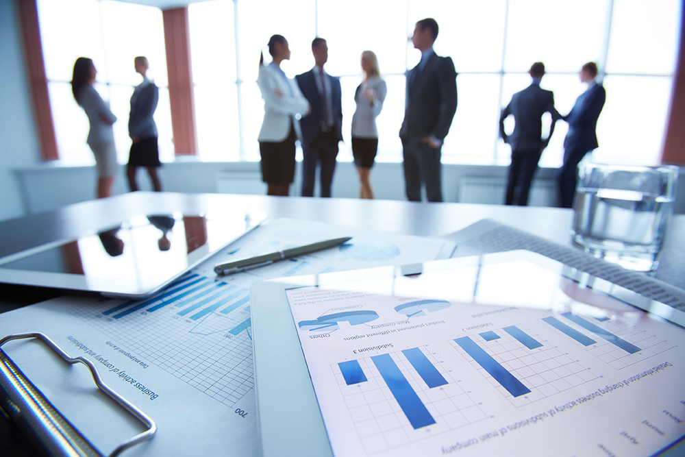 A tablet and pen on a desk with a group of business people