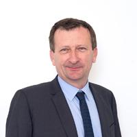 A man in a suit and tie standing in front of a white wall