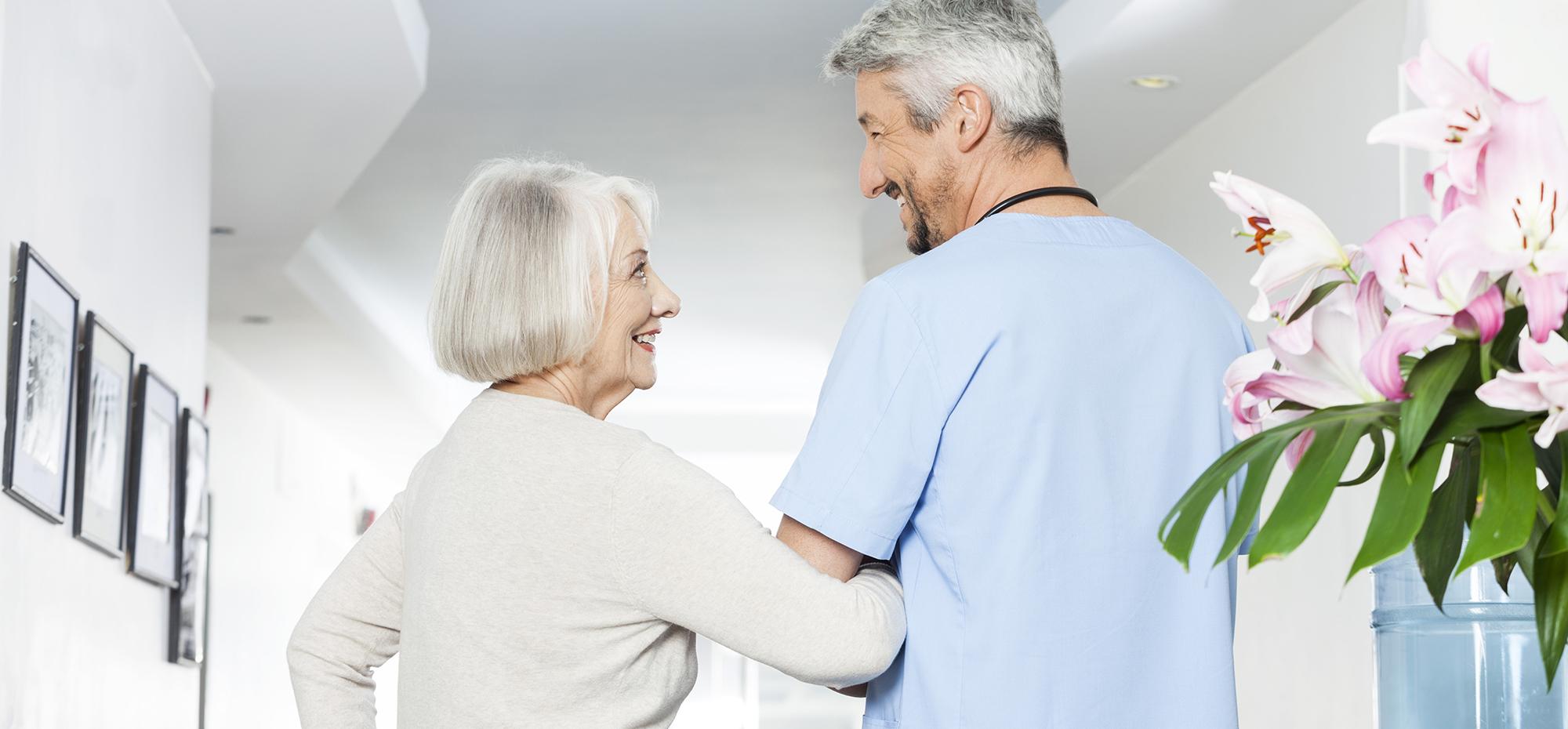 Un aide soignant et une femme âgée se tiennent dans un couloir