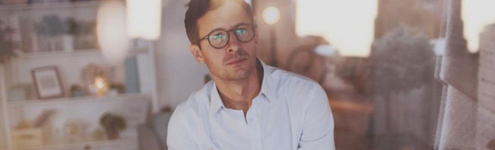 Un homme en lunettes debout devant une fenêtre.